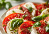 Salade Caprese Italienne : Recette Facile et Fraîche en 10 Minutes Salade caprese colorée composée de tranches de tomates et mozzarella fraîche, feuilles de basilic et filet d’huile d’olive, dressée sur une grande assiette.