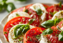 Salade caprese colorée composée de tranches de tomates et mozzarella fraîche, feuilles de basilic et filet d’huile d’olive, dressée sur une grande assiette.