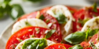 Salade caprese colorée composée de tranches de tomates et mozzarella fraîche, feuilles de basilic et filet d’huile d’olive, dressée sur une grande assiette.