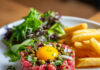 Steak tartare classique Assiette de steak tartare classique au couteau, accompagné de frites maison croustillantes et d'une salade verte fraîche.