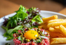 Steak tartare classique Assiette de steak tartare classique au couteau, accompagné de frites maison croustillantes et d'une salade verte fraîche.