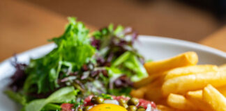 Assiette de steak tartare classique au couteau, accompagné de frites maison croustillantes et d'une salade verte fraîche.