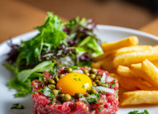 Assiette de steak tartare classique au couteau, accompagné de frites maison croustillantes et d'une salade verte fraîche.