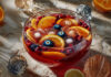Punch d’Halloween fruité et terrifiant Grand saladier de punch d’Halloween rouge sang, garni de rondelles d’agrumes, fruits rouges et d’une main glacée, prêt à être servi.