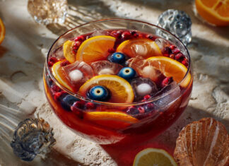 Grand saladier de punch d’Halloween rouge sang, garni de rondelles d’agrumes, fruits rouges et d’une main glacée, prêt à être servi.