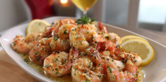 Crevettes rôties à l’ail nappées de beurre citronné, servies chaudes avec du persil frais et quartiers de citron.