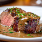 Filet mignon de porc servi en tranches épaisses, nappé d’une sauce crémeuse au porto, parsemé de persil frais sur une assiette blanche.