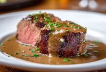 Filet mignon à la sauce au porto Filet mignon de porc servi en tranches épaisses, nappé d’une sauce crémeuse au porto, parsemé de persil frais sur une assiette blanche.