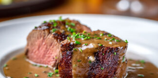 Filet mignon de porc servi en tranches épaisses, nappé d’une sauce crémeuse au porto, parsemé de persil frais sur une assiette blanche.