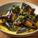 Bol de moules de bouchot nappées de sauce crémeuse au curry et au vin blanc, typique de la mouclade charentaise.