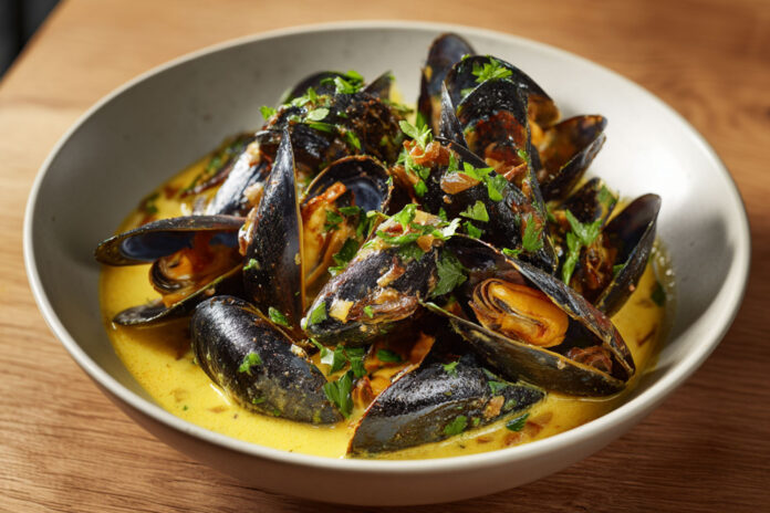 Bol de moules de bouchot nappées de sauce crémeuse au curry et au vin blanc, typique de la mouclade charentaise.