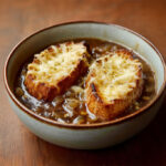 Bol de soupe à l’oignon gratinée avec tranches de pain dorées et fromage fondu – une recette française traditionnelle et réconfortante.
