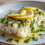 Dos de cabillaud cuit au four, nappé d’huile d’olive citronnée avec ail et persil frais, décoré de rondelles de citron.