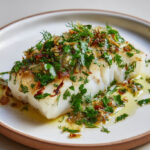 Dos de cabillaud cuit au four, nappé de citron confit haché et d’herbes fraîches, dans une sauce légère à l’huile d’olive.