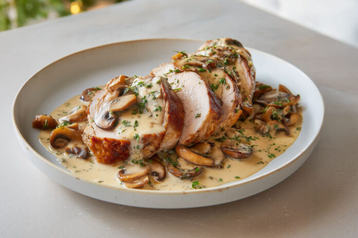 Filet mignon de porc tranché, nappé de sauce crémeuse aux champignons, servi dans une assiette rustique avec du persil frais.