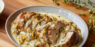 Filet mignon de porc tranché, nappé d’une sauce crémeuse au reblochon et d’oignons confits caramélisés, servi dans une assiette rustique.