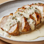 Filet mignon de porc tranché, nappé d’une sauce blanche crémeuse au roquefort, servi chaud dans une assiette rustique.