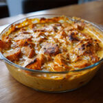 Gratin de patates douces fondant à la crème de coco et au curry, doré au four, servi dans un plat en verre.