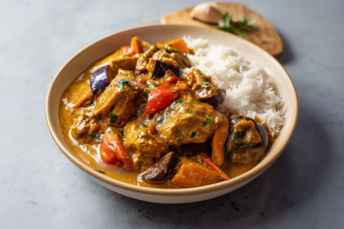 Mafé de poulet sénégalais Assiette de mafé de poulet sénégalais avec carottes, aubergines et patate douce, nappée de sauce onctueuse à la pâte d’arachide, servie avec du riz blanc.