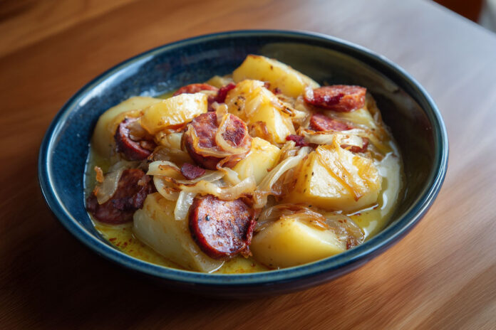 Assiette de ragoût de pommes de terre à l’ardennaise avec saucisse fumée, lardons et oignons caramélisés.