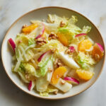 Assiette de salade d’hiver colorée aux endives, quartiers d’orange, pommes croquantes et noix, sur fond clair – recette fraîche et saine.