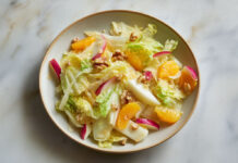 Salade d’hiver aux endives, orange et pomme Assiette de salade d’hiver colorée aux endives, quartiers d’orange, pommes croquantes et noix, sur fond clair – recette fraîche et saine.
