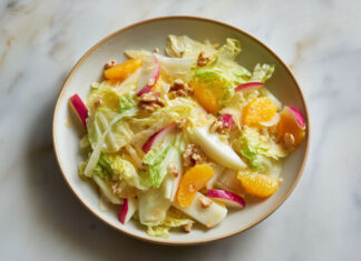 Assiette de salade d’hiver colorée aux endives, quartiers d’orange, pommes croquantes et noix, sur fond clair – recette fraîche et saine.