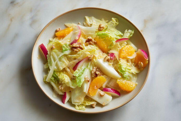 Salade d’hiver aux endives, orange et pomme Assiette de salade d’hiver colorée aux endives, quartiers d’orange, pommes croquantes et noix, sur fond clair – recette fraîche et saine.