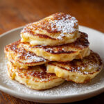 Petites crêpes aux pommes dorées servies chaudes avec sucre glace sur une assiette rustique.