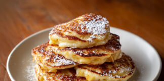 Petites crêpes aux pommes dorées servies chaudes avec sucre glace sur une assiette rustique.